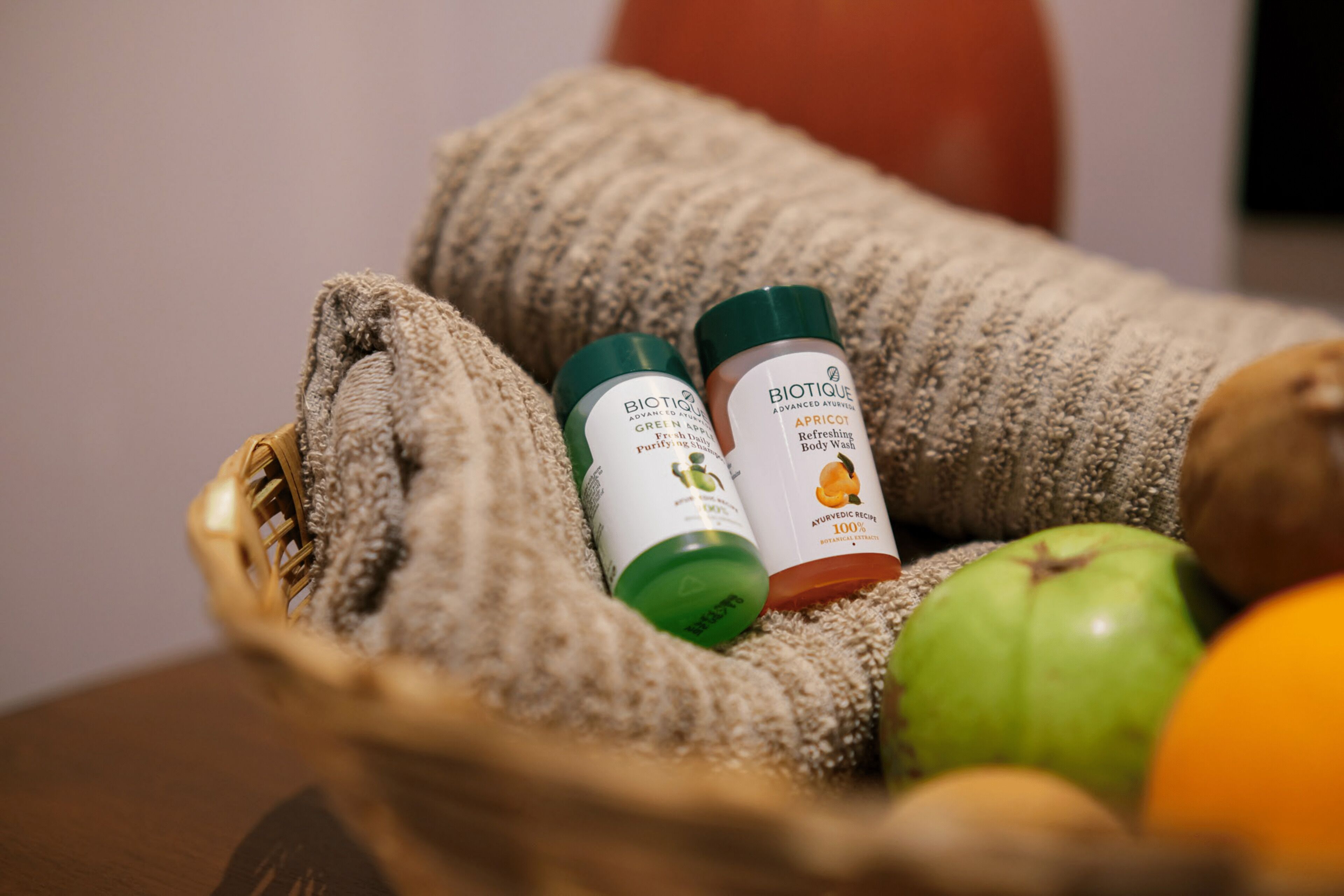 Un panier contenant deux flacons de gel douche Biotique Advanced Aromatic, aux parfums de pomme verte et d’abricot, une pomme verte et une orange.