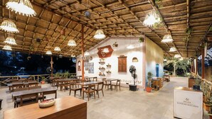 A restaurant with wooden tables and chairs, hanging lights, and a sign for 'MRUDA KONKAN KITCHEN'. - MRUDA FARMSTAY (Dahanu)