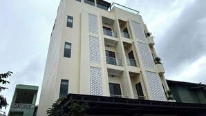 A multi-story building with a distinctive lotus logo at the top, multiple balconies, and a patterned facade. - Bacnam Quang Ngai Hotel (Nghia Lo)