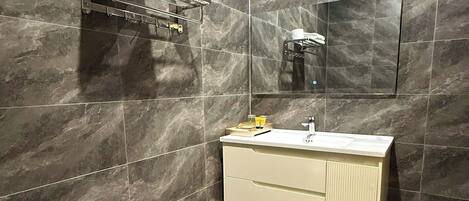 A modern bathroom with dark marble tiles, a white toilet, a beige vanity with a mirror, and a towel rack.