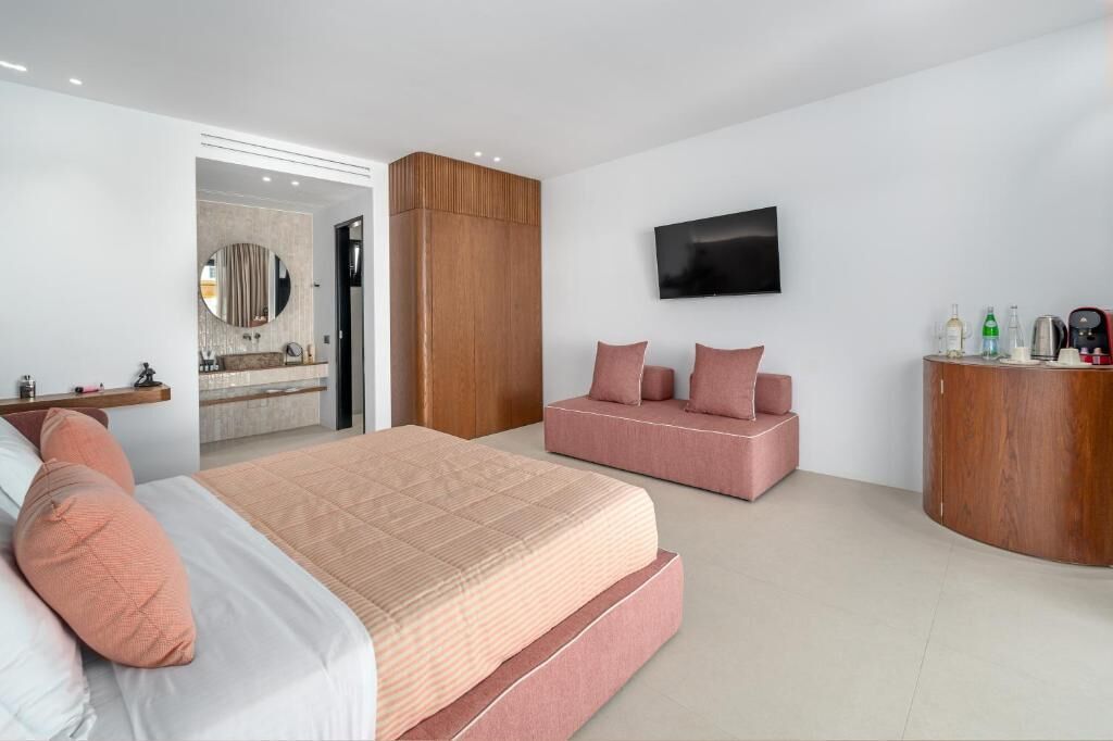 A modern bedroom with a large bed, a seating area, a TV, and a wooden cabinet.