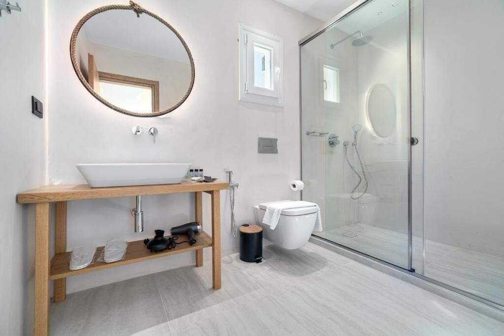 A modern bathroom with a wooden vanity, a round mirror, a glass shower enclosure, and a white toilet.