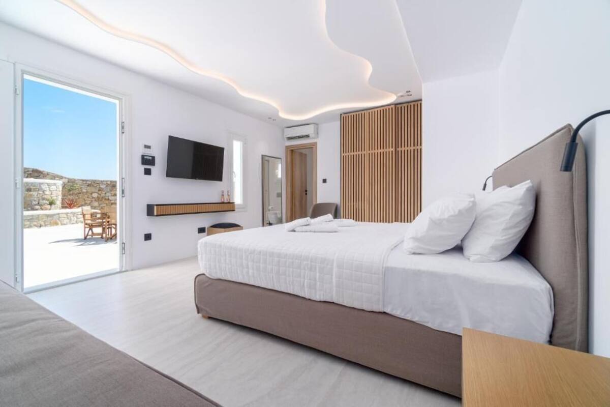 Une chambre moderne dotée d’un grand lit, d’un téléviseur à écran plat et d’une porte-fenêtre coulissante donnant sur un espace extérieur.
