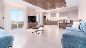 Un salón moderno con un sofá grande, una televisión y una zona de cocina al fondo.