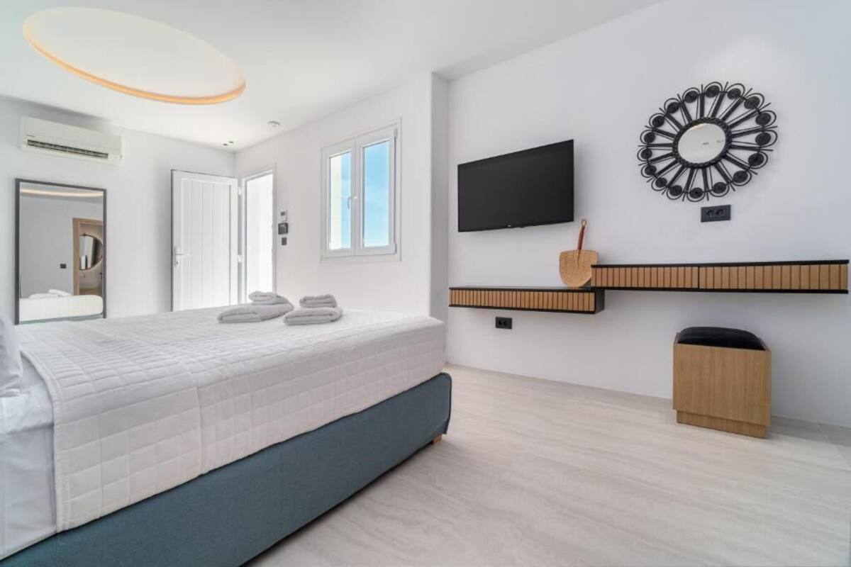 Une chambre moderne avec un lit, une télévision, un miroir et une étagère fixée au mur.