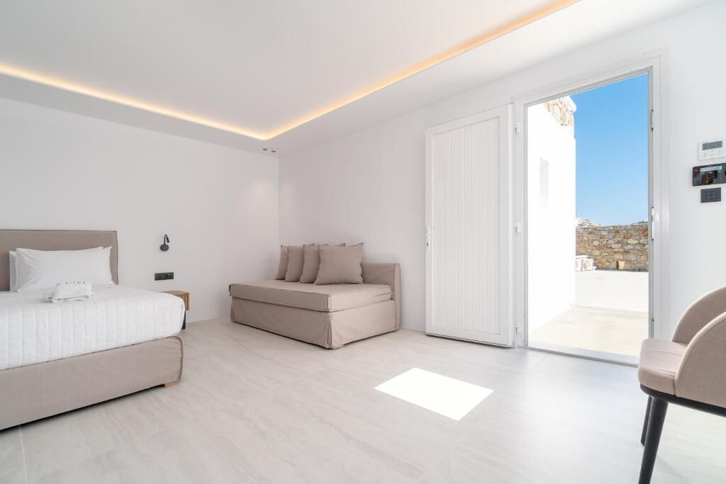 A modern bedroom with a bed, a sofa, and a sliding glass door leading to an outdoor area.
