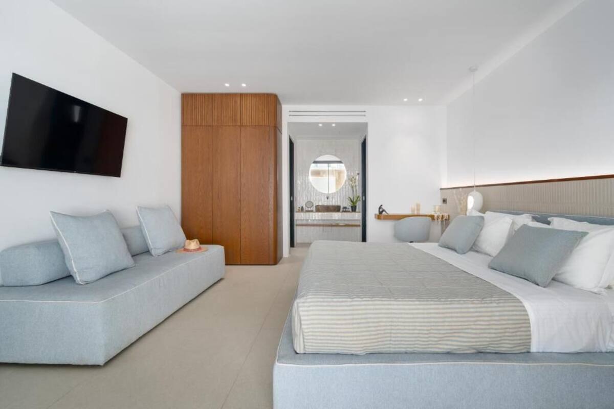 Une chambre moderne avec un grand lit, un canapé et un téléviseur fixé au mur.