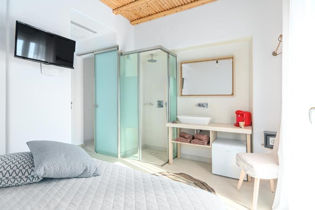 A modern bedroom with a bed, a TV, a glass-enclosed shower, a sink, and a chair.