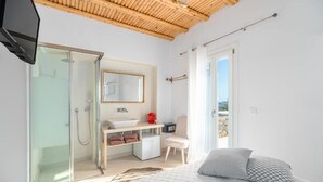 Un dormitorio moderno con una cama grande, cabina de ducha de vidrio, tocador con lavabo y vistas al exterior.