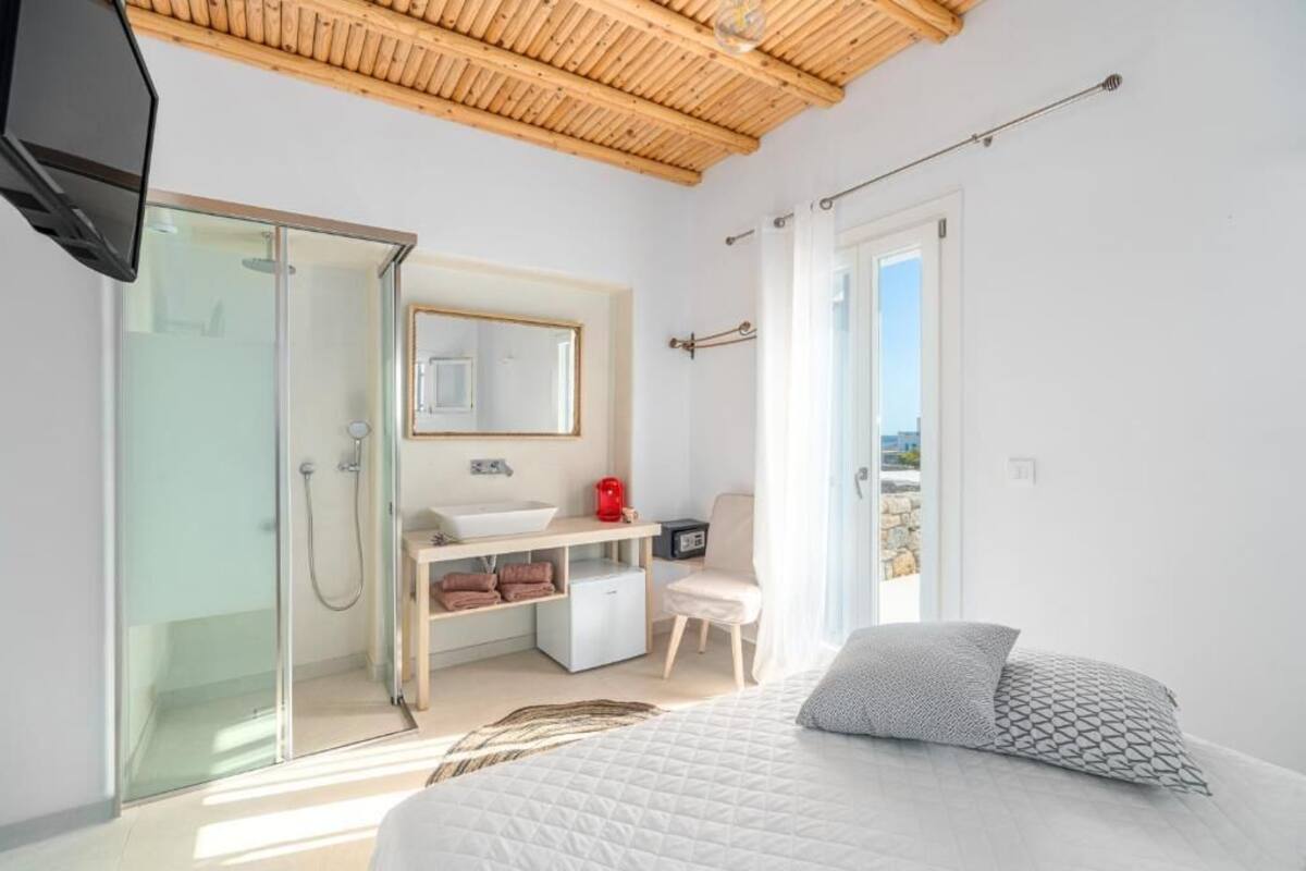 Une chambre à coucher moderne avec un grand lit, une douche en verre, une coiffeuse avec un lavabo et une vue sur l’extérieur.