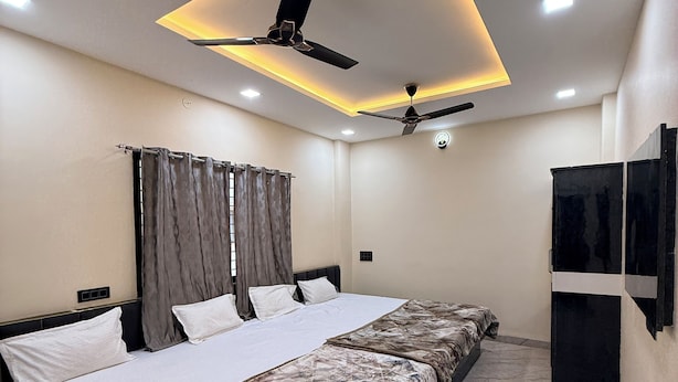 A modern hotel room with a large bed, ceiling fans, recessed lighting, and a flat-screen TV mounted on the wall. - hotel shivlok inn (Ujjain)