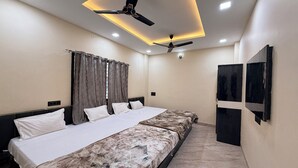 A hotel room with a large bed, ceiling fans, recessed lighting, a window with curtains, and a wall-mounted TV. - hotel shivlok inn (Ujjain)