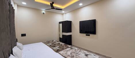 A bedroom with a bed, ceiling fan, recessed lighting, wardrobe, and a wall-mounted TV.
