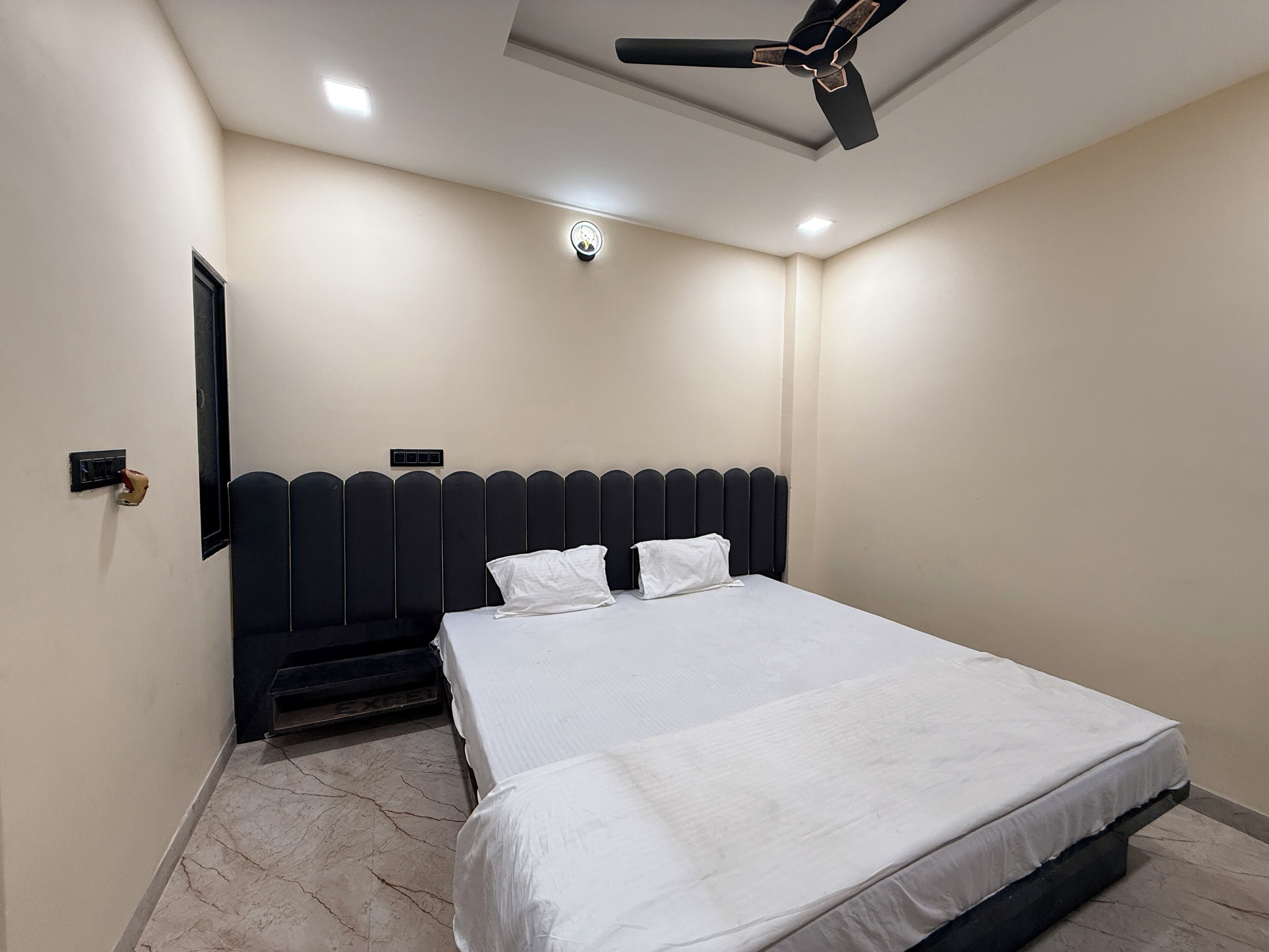 A bedroom with a bed, a ceiling fan, a light fixture, and a door with a handle.