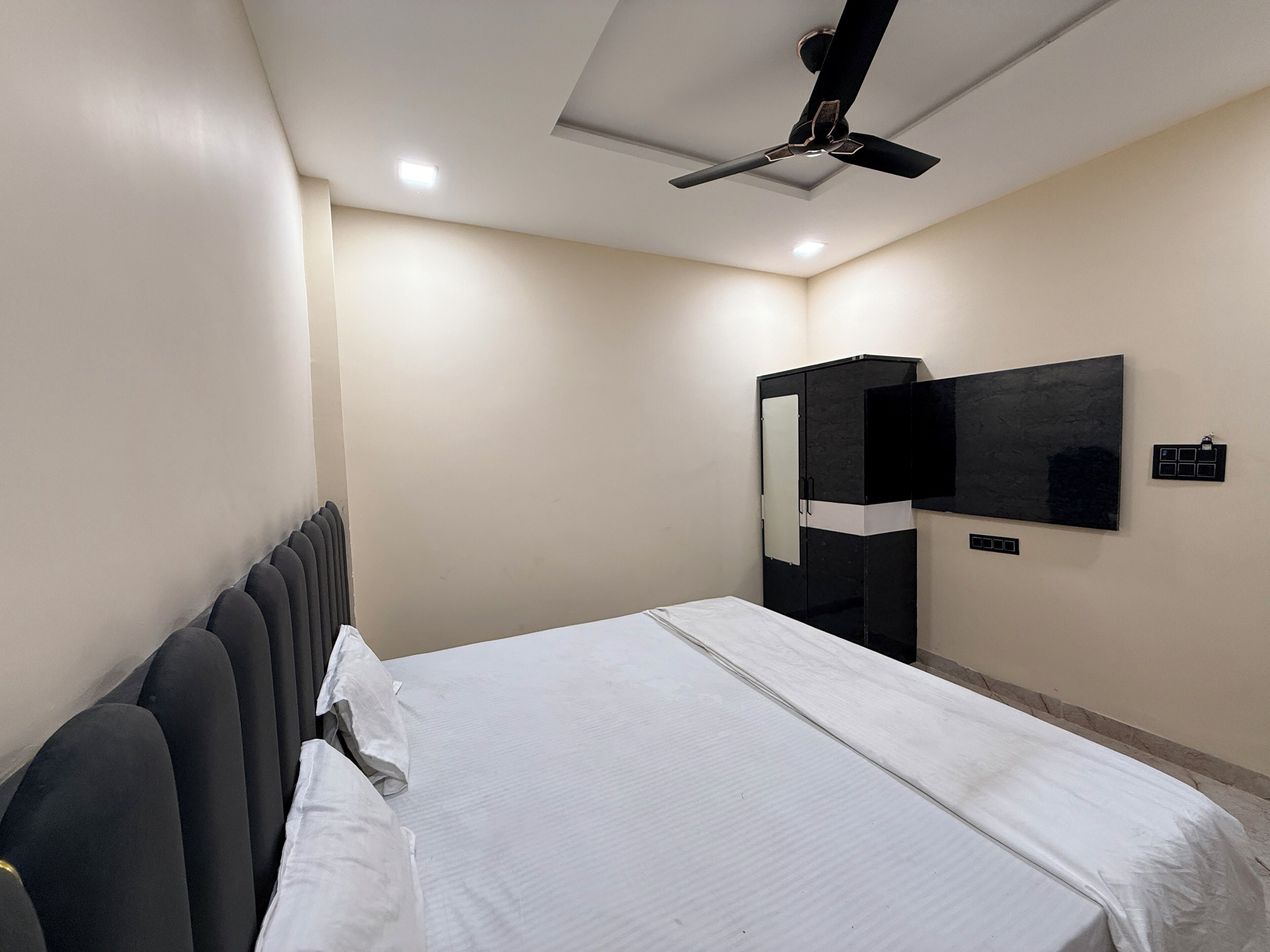 A hotel room with a bed, a ceiling fan, a wardrobe, and a flat-screen TV mounted on the wall.
