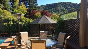 Eine Terrasse mit Tisch und Stühlen, eine Pergola und Blick auf einen Pool und bewaldete Hügel.