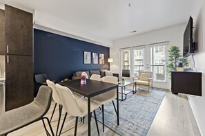 Una sala moderna con comedor, una pared de acento azul oscuro y un ventanal con persianas.