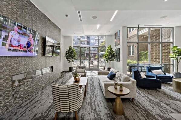 A modern hotel lobby with a seating area, a TV mounted on the wall, and a view of the outside.