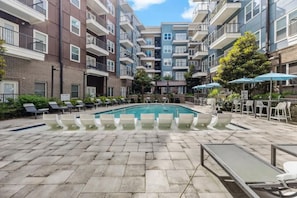 Una piscina con sillones de playa y sombrillas, rodeada de edificios residenciales de varios pisos.