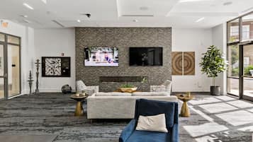 A modern lobby with a sofa, a TV mounted on a textured wall, and a potted plant.