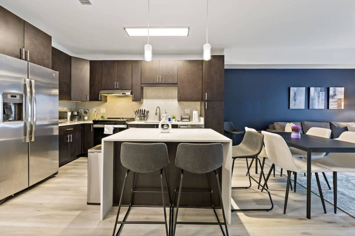 A modern kitchen with a central island, bar stools, and a dining area with a table and chairs.
