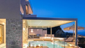 Un espace piscine extérieur moderne, doté d’une structure en verre, de murs en pierre et de coins salon aménagés à l’extérieur.