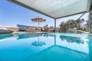 A swimming pool with clear blue water, a covered seating area, and a view of trees and a building in the background. - Isle of View Villa - Lefkada (Lefkada)