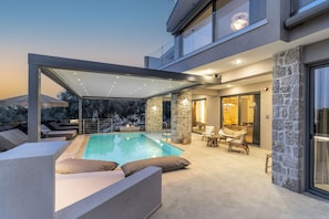 A modern outdoor pool area with a glass enclosure, stone pillars, and lounge furniture. - Isle of View Villa - Lefkada (Lefkada)