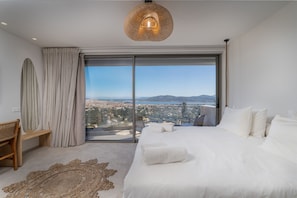 A bedroom with a large bed, a view of a cityscape through a sliding glass door, and a woven rug on the floor. - Isle of View Villa - Lefkada (Lefkada)