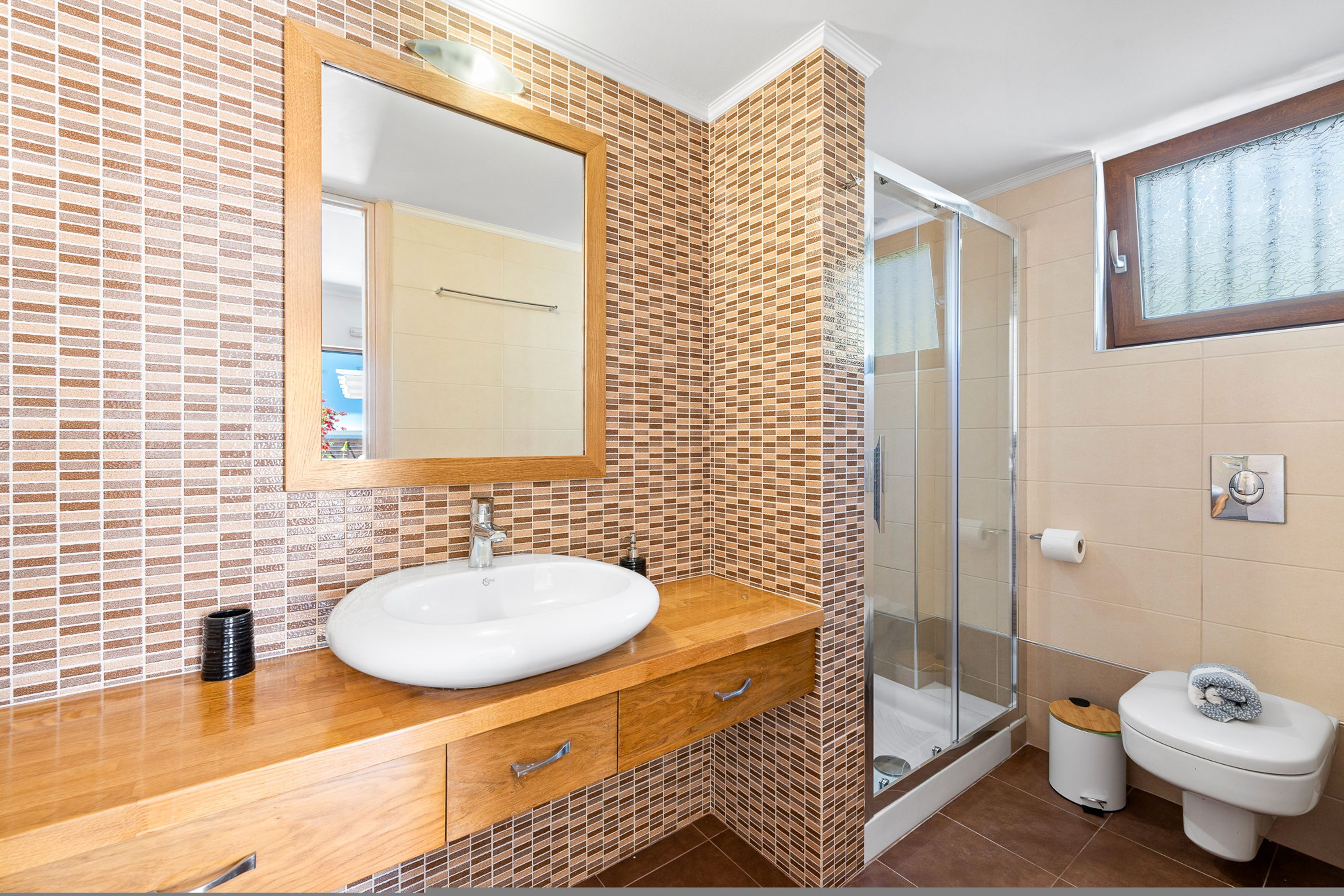 A bathroom with a wooden vanity, a white sink, a mirror, a glass shower enclosure, and a toilet.
