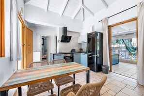 Une cuisine moderne avec un réfrigérateur noir, une table à manger en bois et quatre chaises, et une vue sur le balcon extérieur.