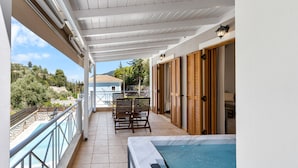 Un balcón con hidromasaje, una mesa con sillas y vistas a una piscina y vegetación.