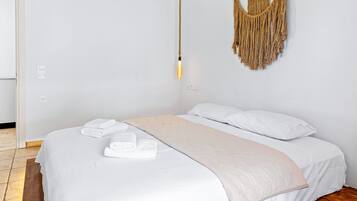 A bedroom with a large bed, white bedding, a macrame wall hanging, and a hanging light fixture.