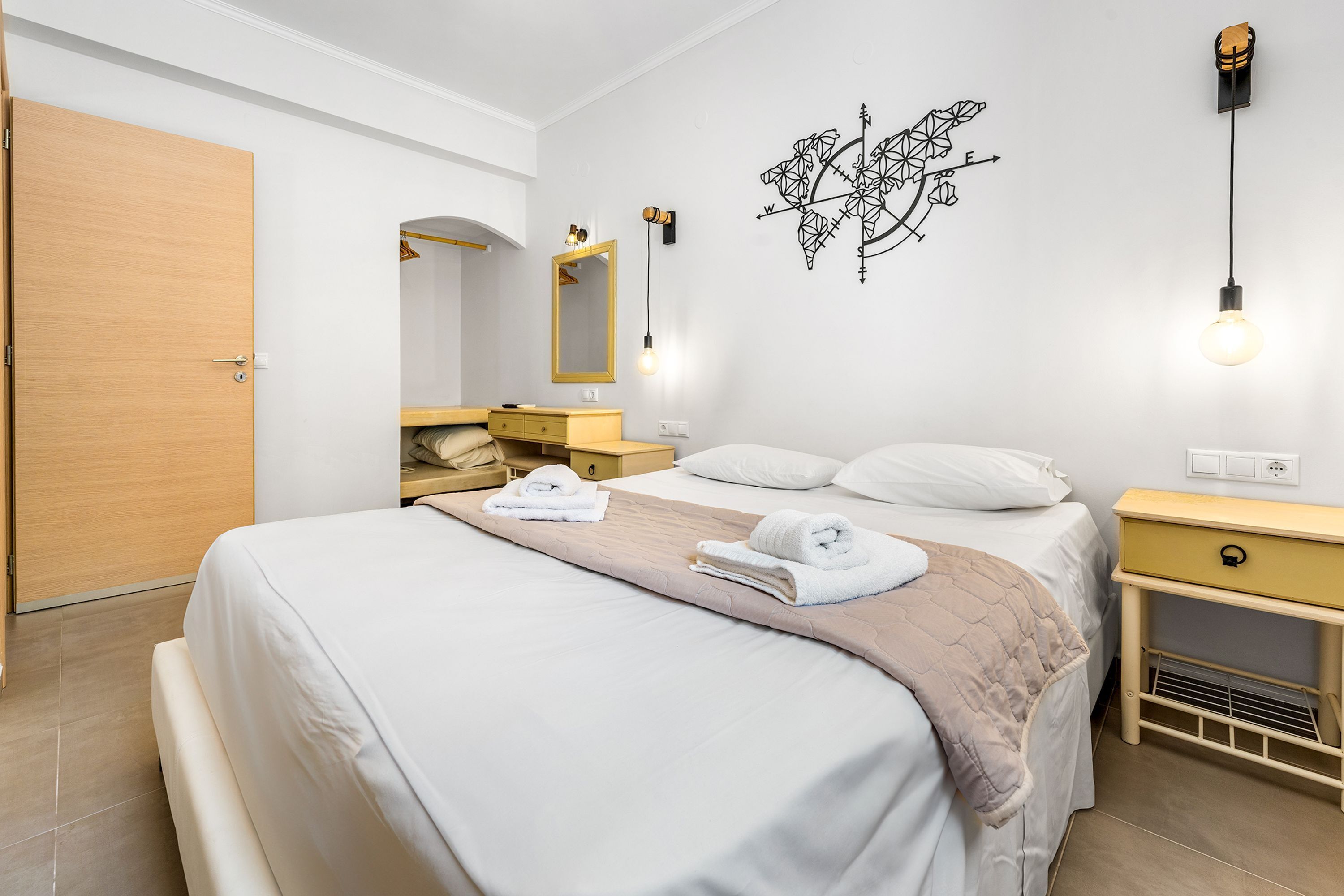 Quarto de hotel bem organizado, com cama, mesas de cabeceira, guarda-roupa e espelho.
