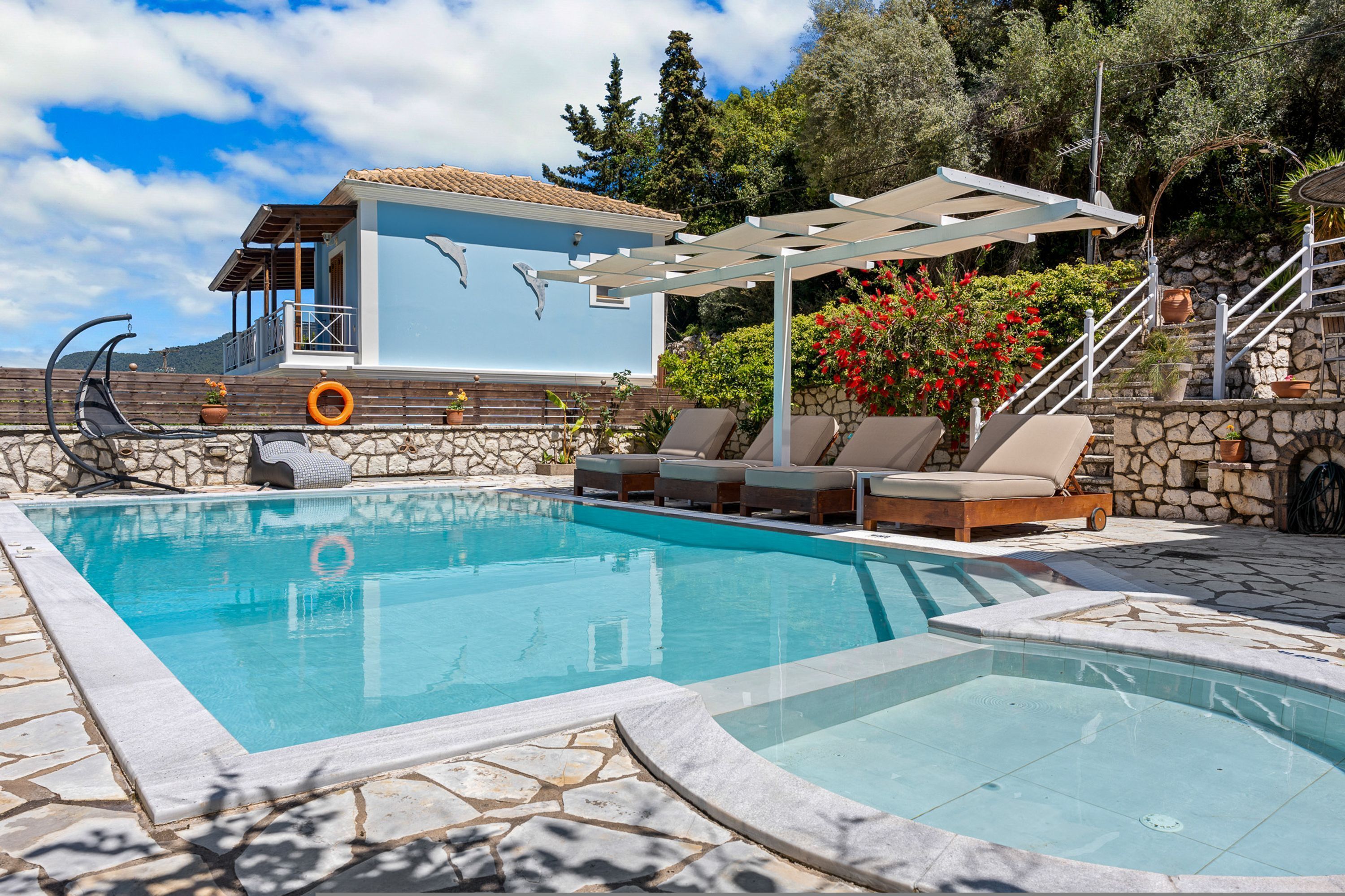 A swimming pool with lounge chairs and a pergola, surrounded by stone walls and potted plants.