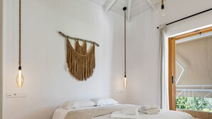 A bedroom with a wooden platform bed, white linens, a macramé wall hanging, and a view through a large window. - Villa Semipuella (Lefkada)
