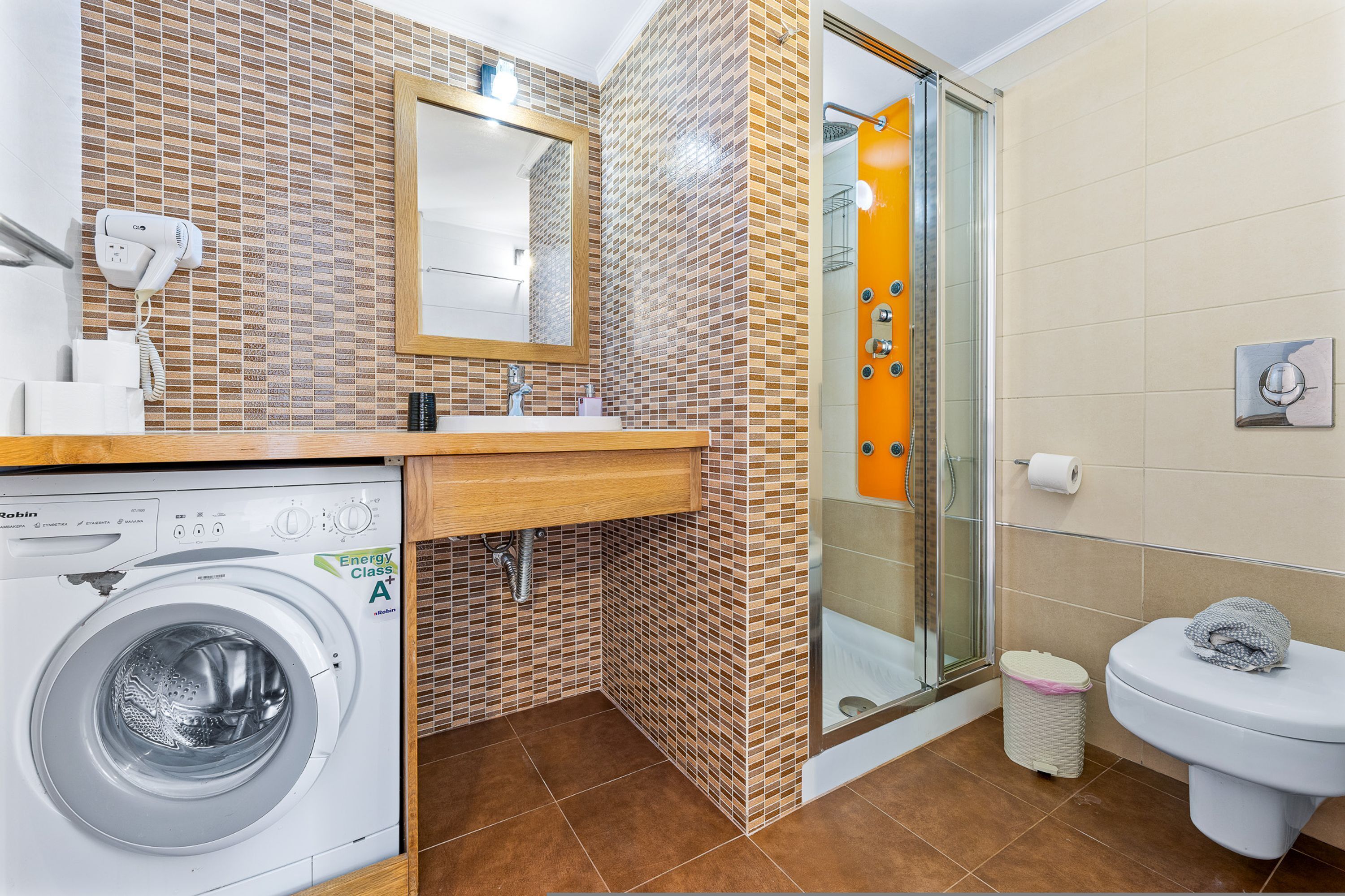 A compact bathroom with a washing machine, a sink, a toilet, and a shower area.