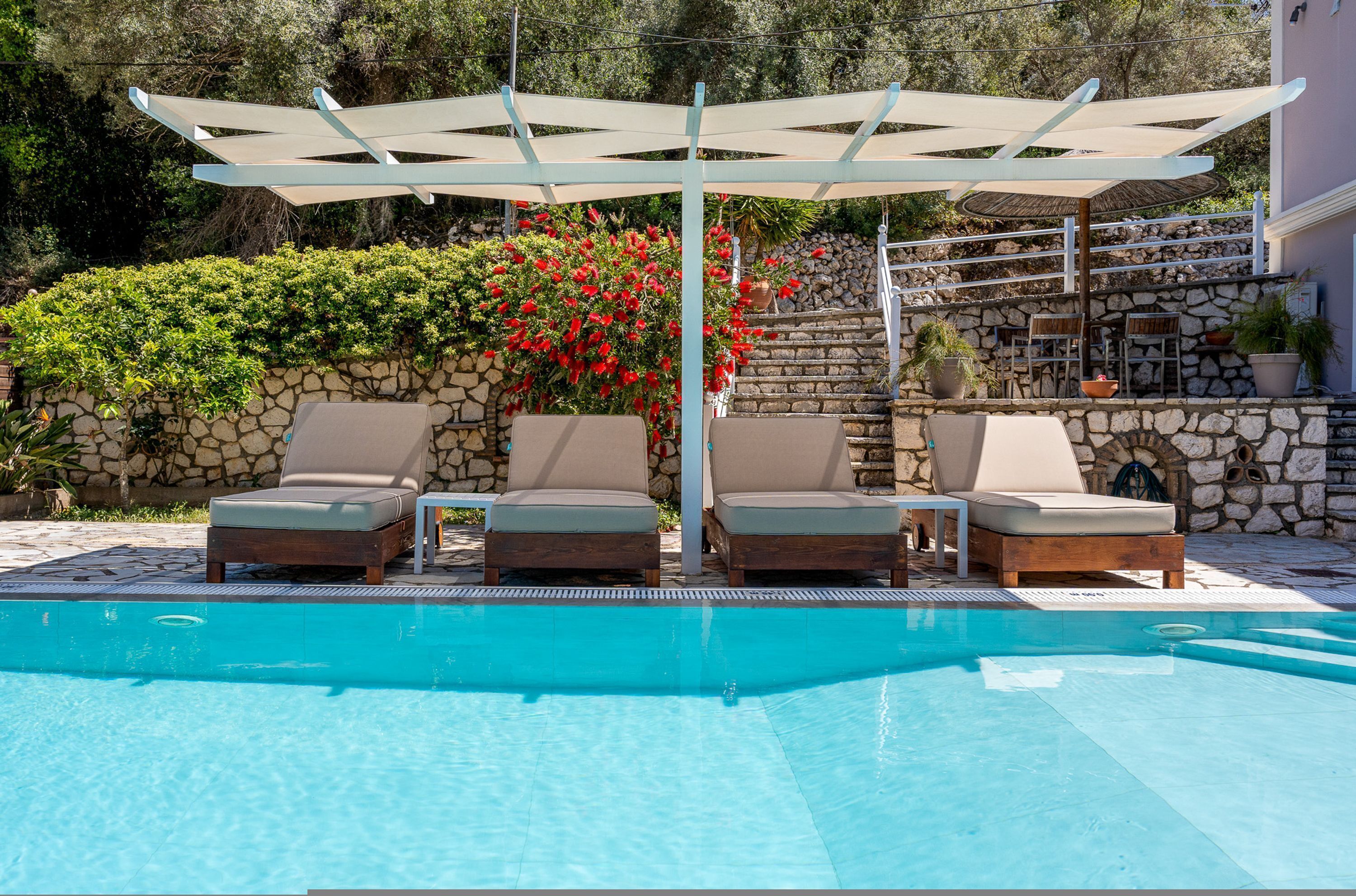 A poolside area with lounge chairs, a pergola, and a stone wall.