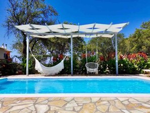 Ein Poolbereich mit weißer Pergola, einer Hängematte und einem Schaukelstuhl.