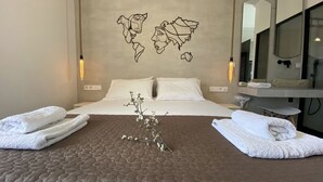 A hotel room with a large bed, two white pillows, a brown textured bedspread, a decorative branch, and towels on either side of the bed. - Ninfas del Mar (Lefkada)