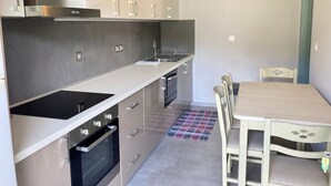 A modern kitchen with stainless steel appliances, a dining table with chairs, and a patterned rug on the floor. - Sea Breeze Apartment n 2 (Lefkada)
