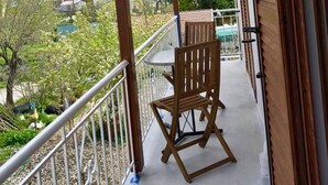 A balcony with a wooden chair and table, overlooking a mountainous landscape with houses. - Sea Breeze Apartment n 2 (Lefkada)