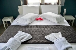 A neatly made bed with white pillows and a grey quilted blanket, two small bedside tables, and a pair of red roses on the pillows. - Sea Breeze Apartment n 2 (Lefkada)