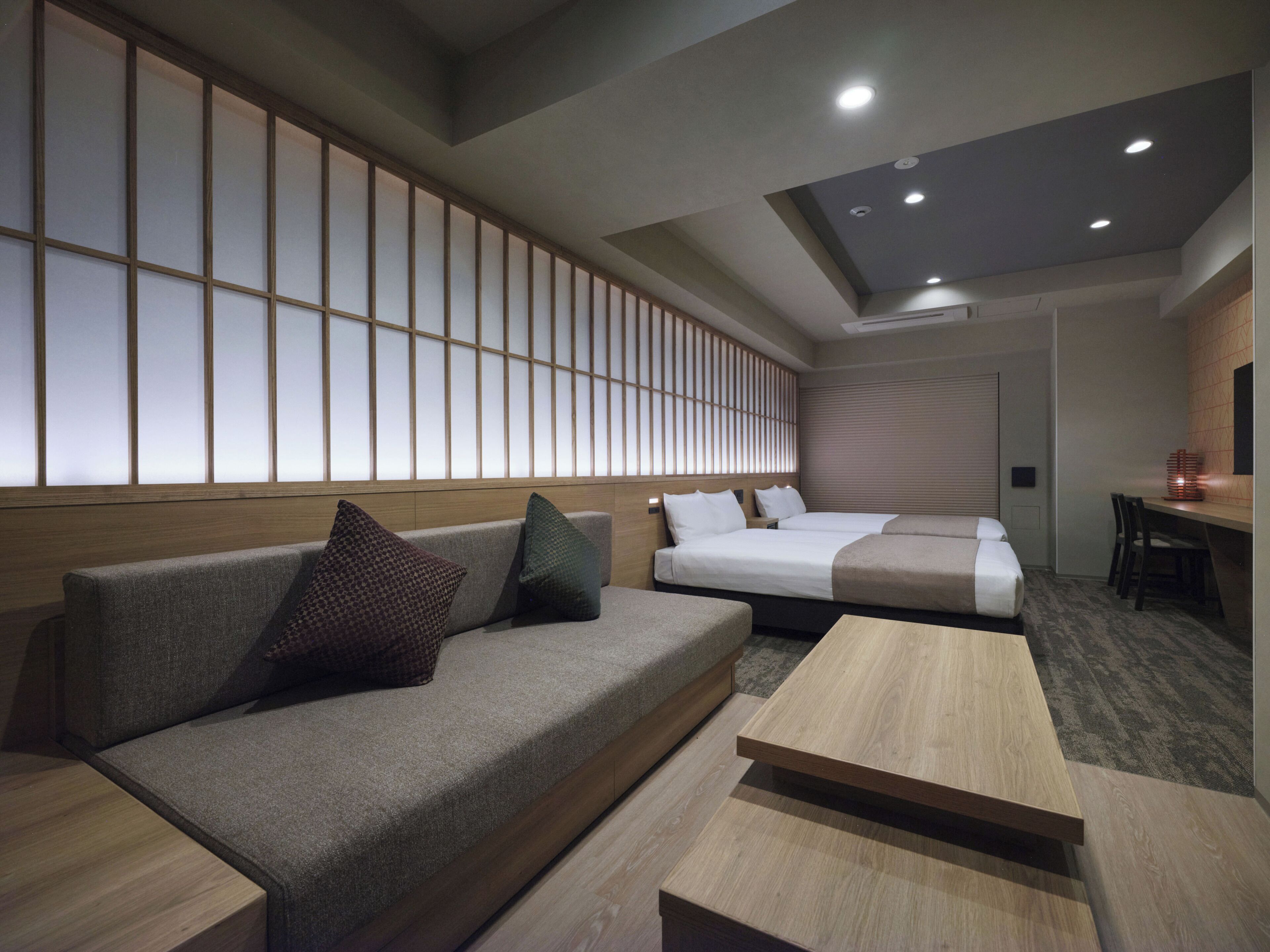 A modern hotel room with a sofa, two beds, a wooden coffee table, and a large window with a view.