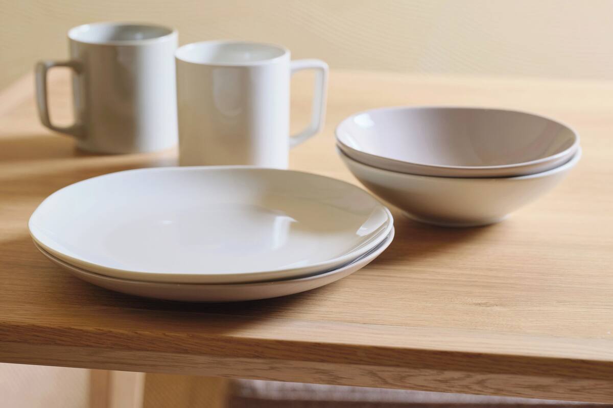 Una mesa de madera con tres platos de cerámica blanca y dos tazas de cerámica blanca.