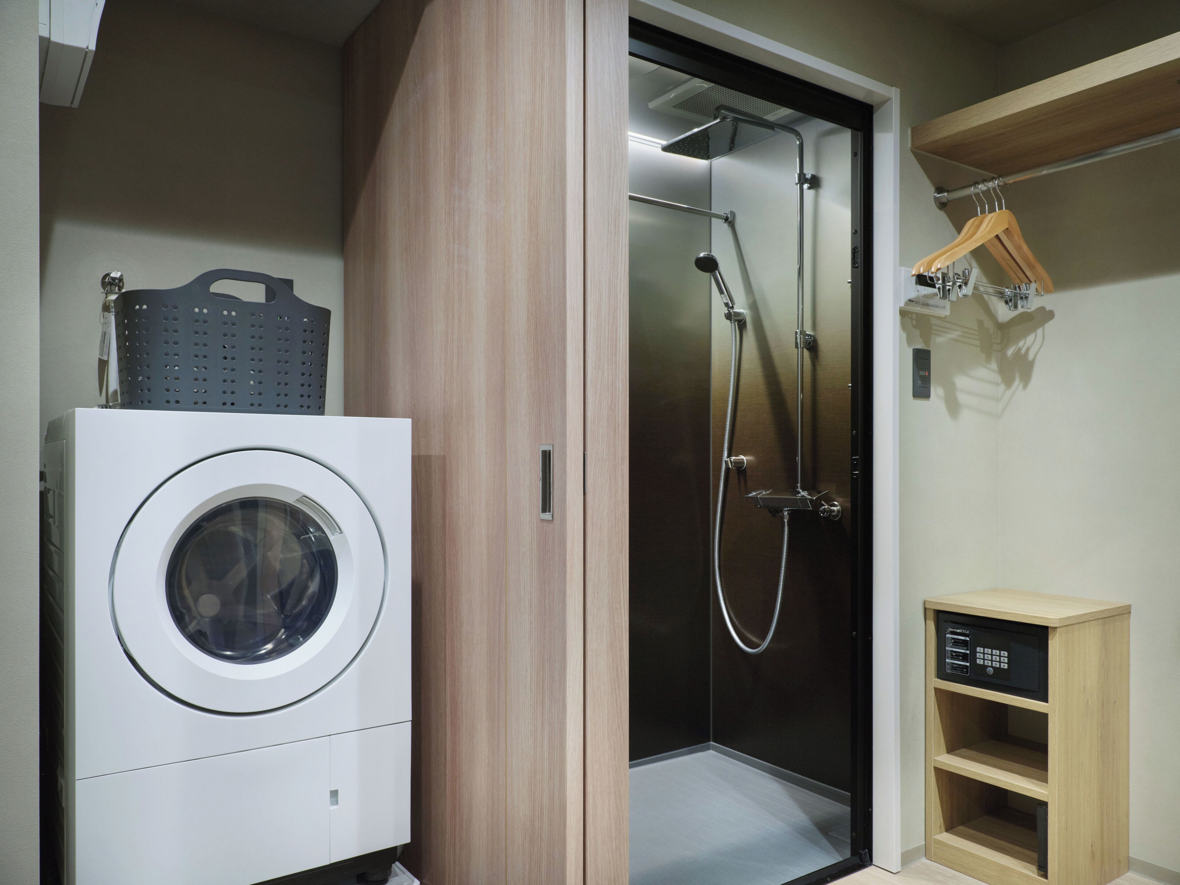 Een compacte kamer met een wasmachine, een douchecabine en een klein houten kastje.