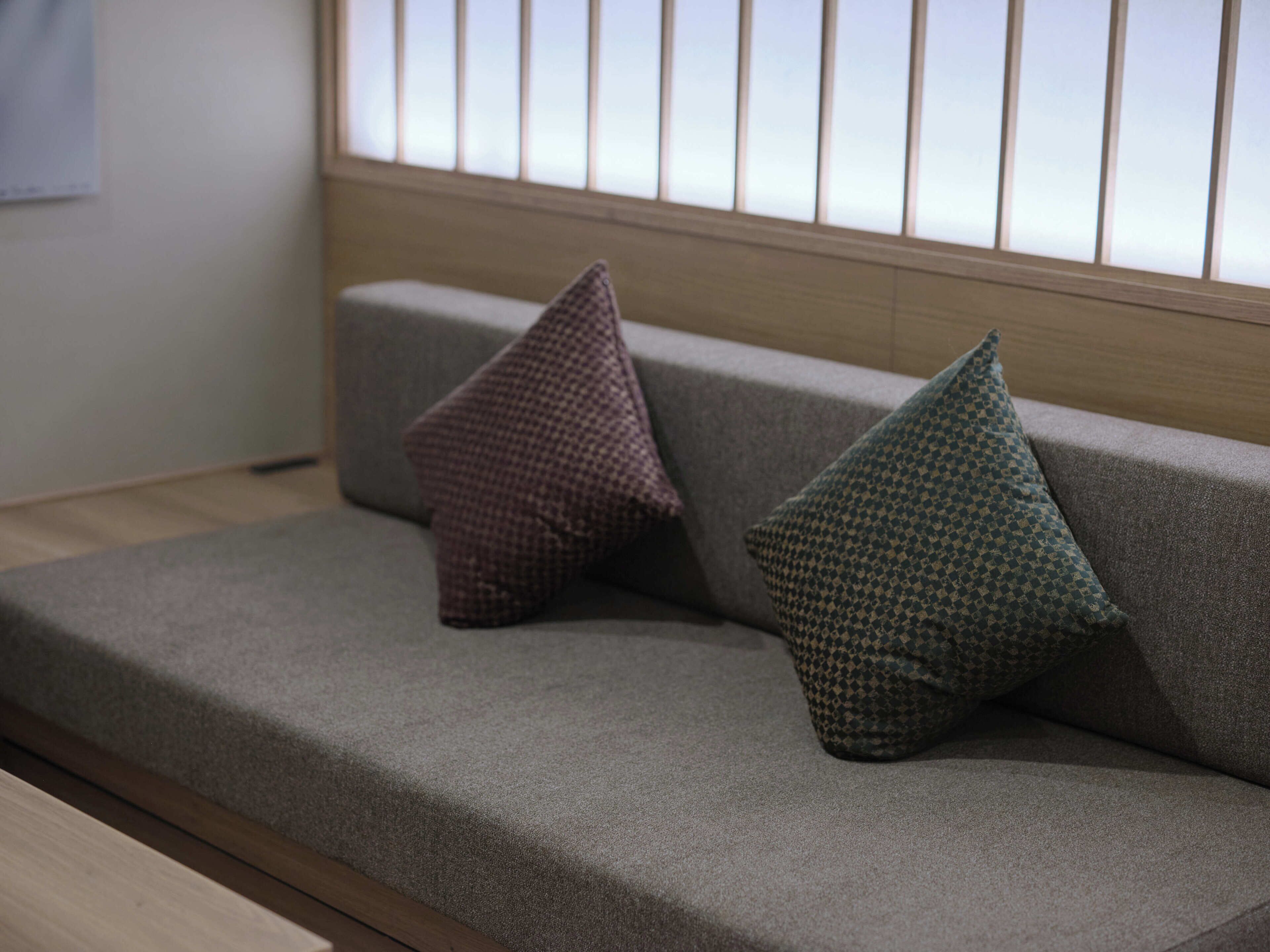 Un sofá con dos almohadas y una ventana con persianas.