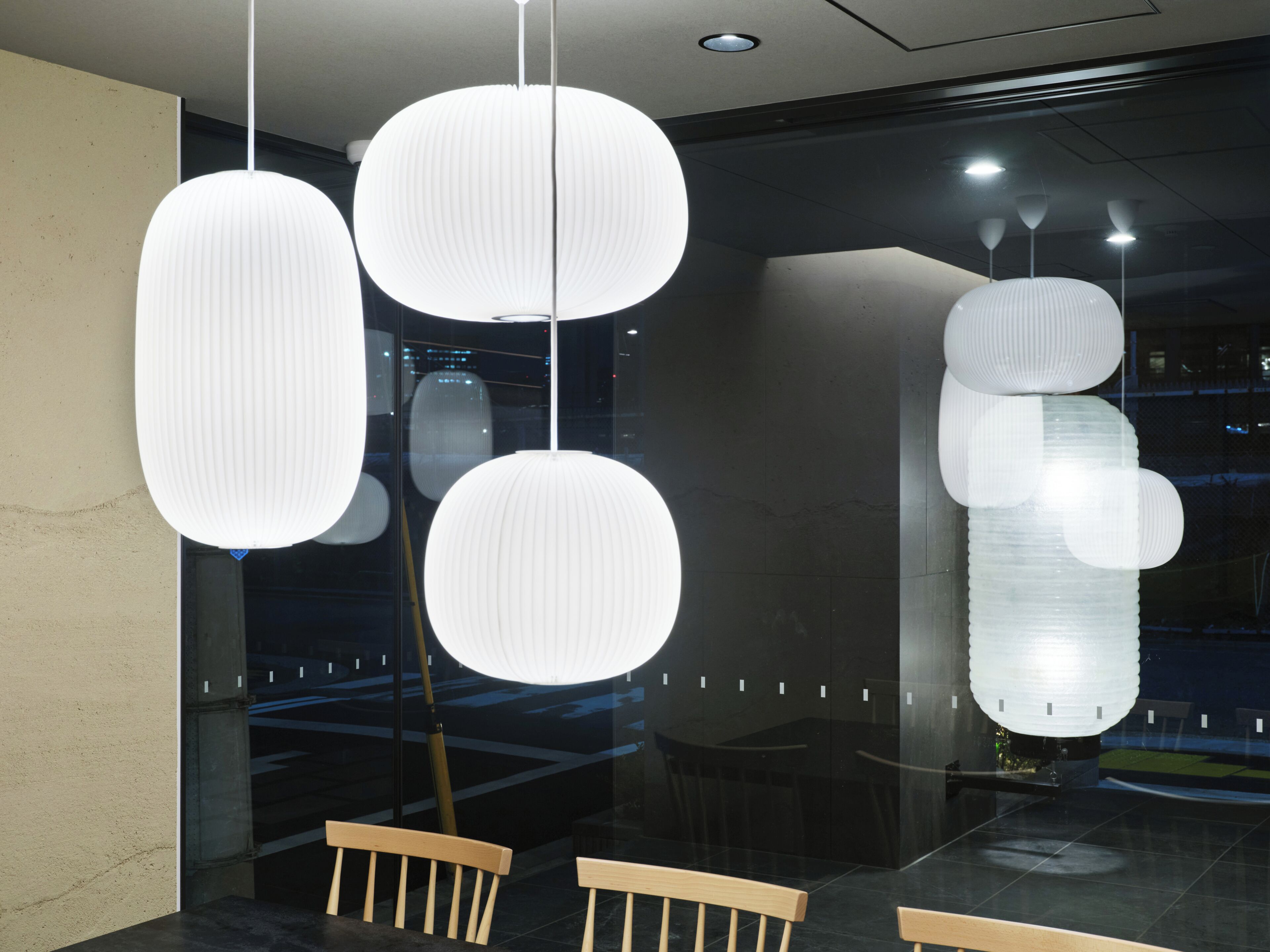 A modern interior with hanging spherical light fixtures, wooden benches, and a glass partition.