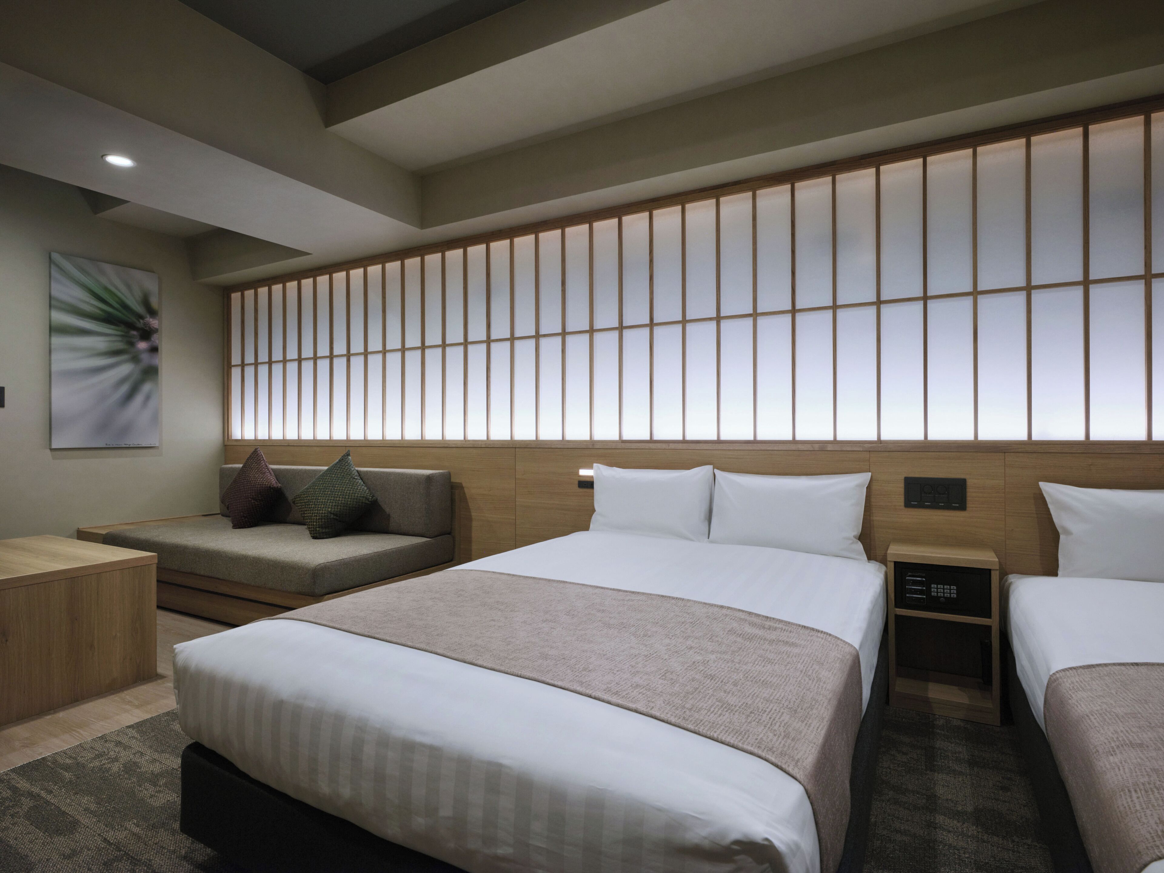A hotel room with a large bed, a smaller bed, a sofa, and a nightstand with a lamp.
