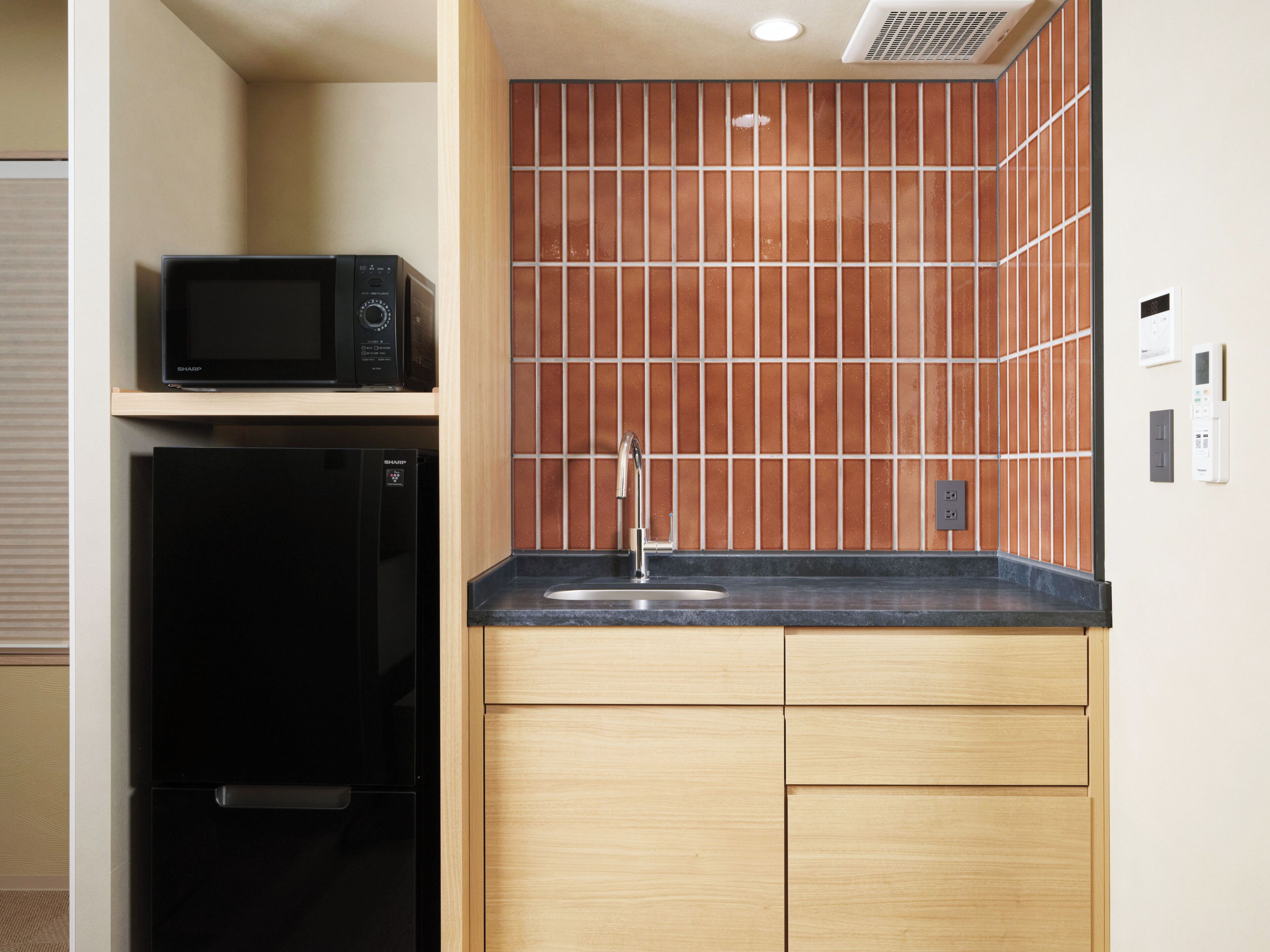 A compact kitchen with a microwave, refrigerator, and a tiled backsplash.